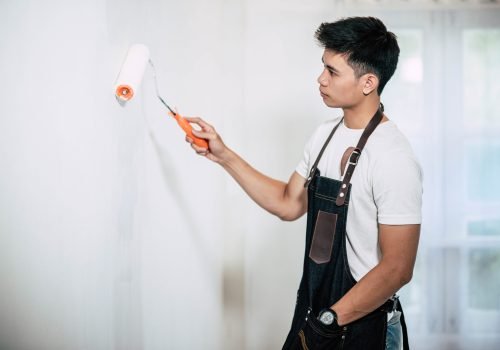 A carpenter holds a paintbrush and paints wood. Selective focus.
